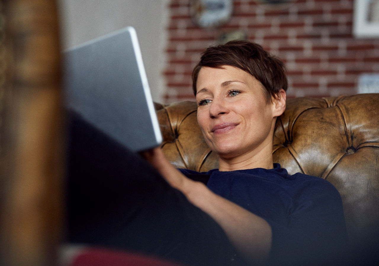woman smiling on the sofa looking at the tablet